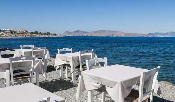 White restaurant tables on the beach in summer - travel, vacation and summer concept. The perfect lunch with a sea view