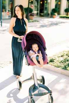 Mom with a baby in a stroller stands on the sidewalk. High quality photo
