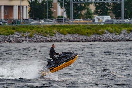 Russia, St. Petersburg, 29 July 2022: a man in a wetsuit rides a jet ski in sunny weather, jumps and has fun, splashes of water, embankment in the background. High quality photo