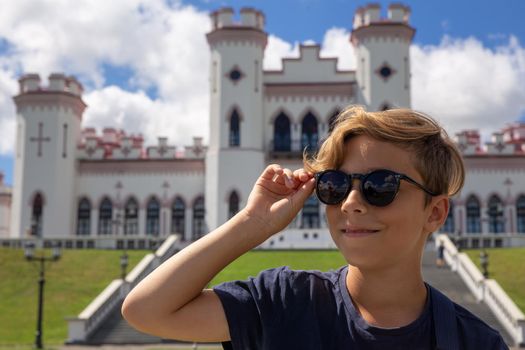 Beautiful stylish 9 years old boy posing with sun glasses and smiling over ancient castle in Belarus Young tourist looking at historical attractions.