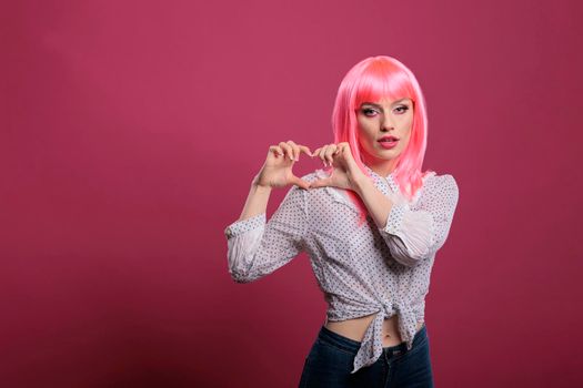 Positive person showing romantic heart shaped sign on camera, doing sincere love gesture with hands. Expressing romance and feelings on valentines day, beautiful symbol over pink background.