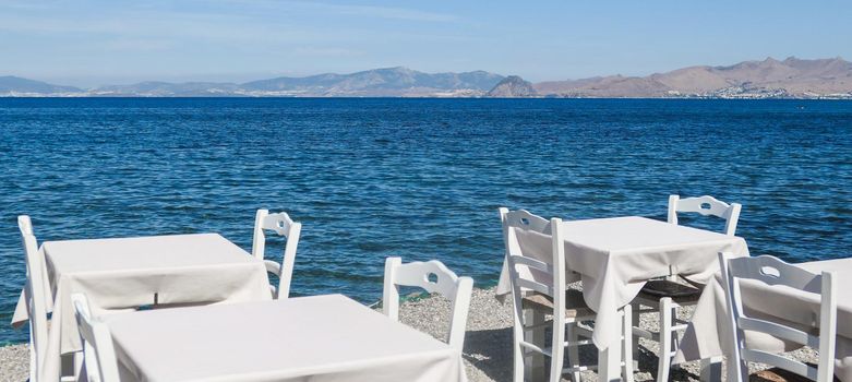 White restaurant tables on the beach in summer - travel, vacation and summer concept. The perfect lunch with a sea view