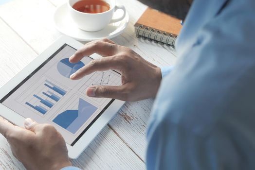 man's hand working on digital tablet at office desk, using self created chart.