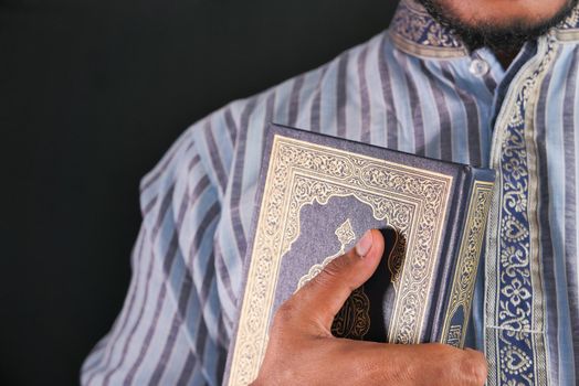Muslim man hand holding Quran isolated on black .