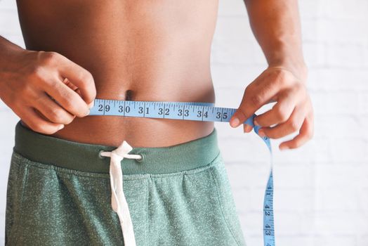 young man measuring his waist with a tape measure, close up