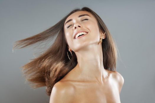 Beautiful brunette girl with hair in the air, studio portrait. Happy smiling face expression.