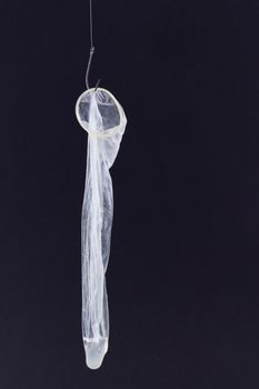 Used Condom with Sperm Inside is Hanging on a Fishing Hook Against the Black Background
