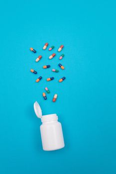 Global Pharmaceutical Industry and Medicinal Products - Colored Pills or Capsules Scattered from the Pill Container, Lying on Blue Background