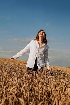 Happy young woman in a white shirt in a wheat field. Sunny day. Girl smiling, happiness concept. Hands to the side. Vertical photo