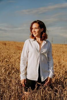 Happy young woman in a white shirt in a wheat field. Sunny day. Girl smiling, happiness concept. Vertical photo