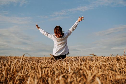 A woman in a white shirt in a rye field. View from the back. The concept of pacification, meditation, happiness, harmony