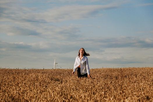 Happy woman in a white shirt runs in a wheat field on a summer day. Happiness and joy concept