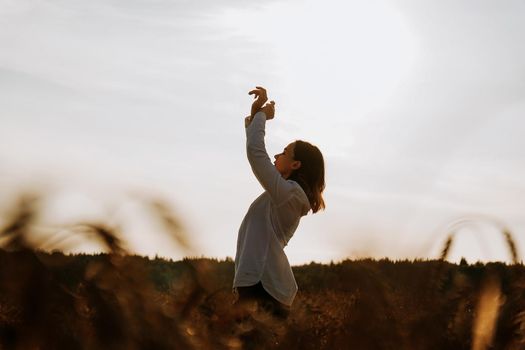 Silhouette of woman enjoying sunset. A woman in a wheat field makes flowing movements. The concept of calmness and meditation