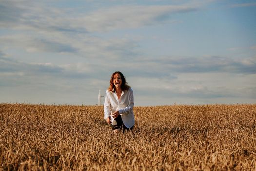 Happy woman in a white shirt runs in a wheat field on a summer day. Happiness and joy concept