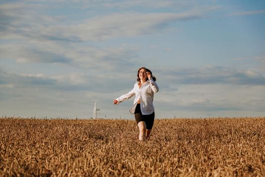 Happy woman in a white shirt runs in a wheat field on a summer day. Happiness and joy concept