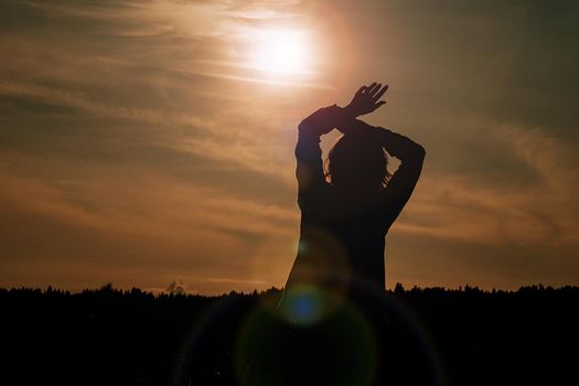 Silhouette of woman enjoying sunset. A woman in a wheat field makes flowing movements. The concept of calmness and meditation