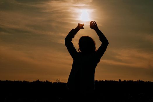 Silhouette of woman enjoying sunset. A woman in a wheat field makes flowing movements. The concept of calmness and meditation