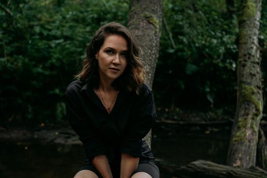 Young woman - close portrait in a dark pine forest. Woman in black shirt