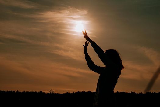 Silhouette of woman enjoying sunset. A woman in a wheat field makes flowing movements. The concept of calmness and meditation