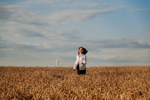 Happy woman in a white shirt runs in a wheat field on a summer day. Happiness and joy concept