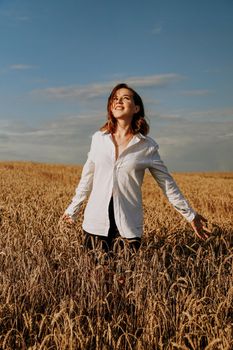 Happy young woman in a white shirt in a wheat field. Sunny day. Girl smiling, happiness concept. Hands to the side. Vertical photo