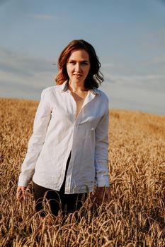 Happy young woman in a white shirt in a wheat field. Sunny day. Girl smiling, happiness concept. Vertical photo