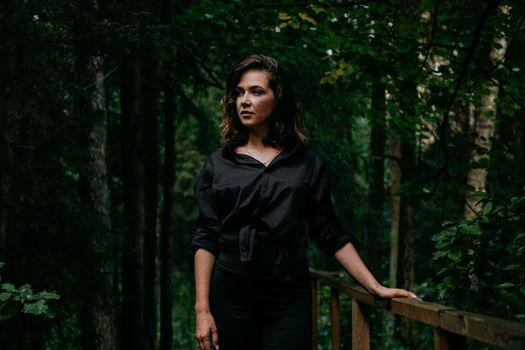 Young woman - close portrait in a dark pine forest. Woman in black shirt