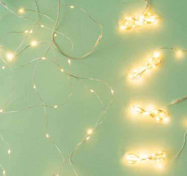 Christmas lights on light green background, flat lay with holiday garland, copy space