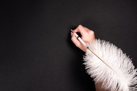 Female hand holding feather pen over black background