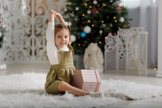 Little smiling girl with new year gift while sitting on the carpet in christmas interior.