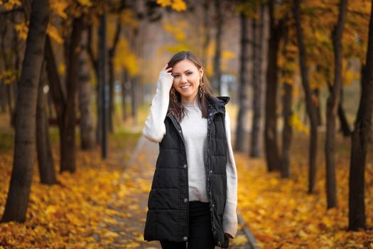 Portrait of a young Central Asian woman in an autumn park on an alley with fallen autumn leaves.