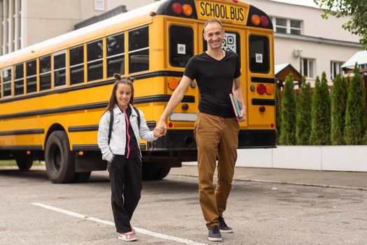 first day at school. father leads a little child school girl in first grade