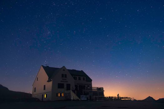 A pub stands alone shortly after the sun sets, with orange skyglow on the horizon as dark blue skies take over, twinkling with stars. Taken at Col d'Aubisque, a mountain pass in the Pyrenees