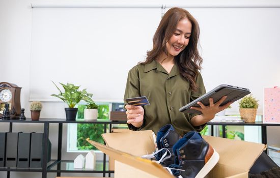 Asian young woman received online shopping parcel opening shoes boxes to checking on digital tablet, Cheerful woman holding credit card, happy female unpacking cardboard box, Shop online and delivery