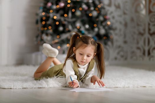 Little girl is writing a letter to santa claus against the background of Christmas trees. Copy space