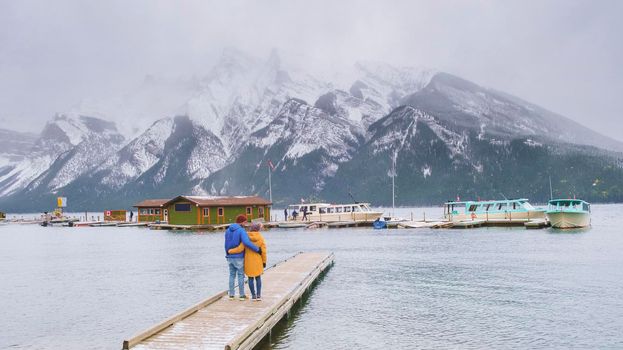 Minnewanka lake in the Canadian Rockies in Banff Alberta Canada with turquoise water, Lake Two Jack in the Rocky Mountains of Canada. a couple of men and women hiking by the lake during snow weather