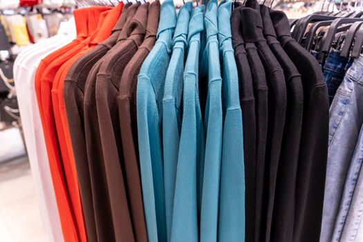 multi colored sweatshirts hang on a hanger in a clothing store. Close-up: Hangers with casual clothes in a mall. Designer clothing collection. New collection in fashion boutique