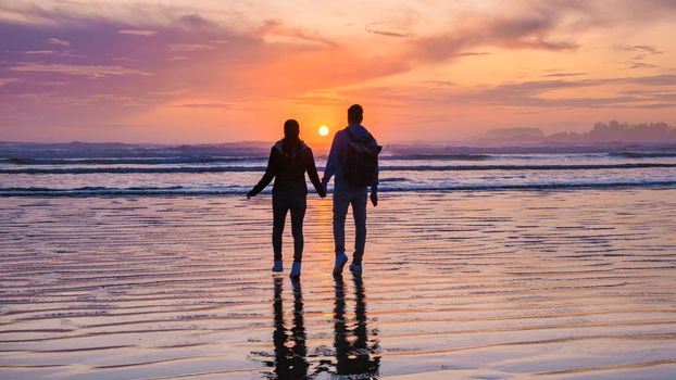 a couple of men and women mid-age watching the sunset on the beach of Tofino Vancouver Island Canada, beautiful sunset on the beach with pink-purple colors in the sky. Canada Tofino Vancouver Island