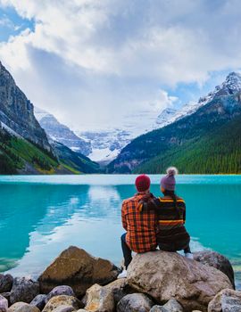 Lake Louise Banff national park is a lake in the Canadian Rocky Mountains. A young couple of men and women sitting on a rock by the lake during a cold day in Autumn in Canada