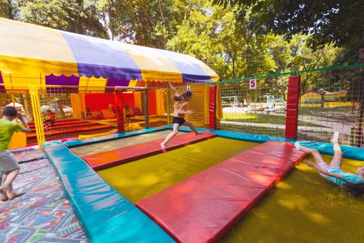 The young children are jumping in the bright trampoline park outdoors in the summer park