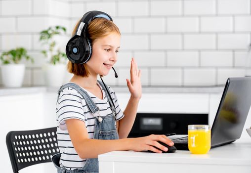 Preteen girl wearing headphones study with laptop. during online lesson at home at pandemic coronavirus. Child pupil making video call with orange juice glass on table