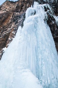 Frozen waterfall on rocky mountain in winter day.