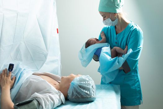 Nurse holds newborn baby close to mother in hospital, seconds after birth.