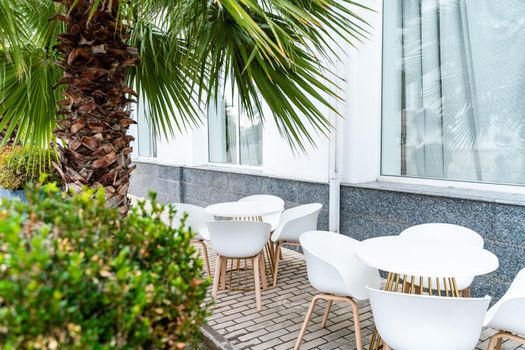 Street cafe with white chairs, green foliage around. Without people, tourism, travel