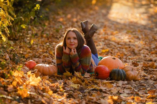 Happy woman with pumpkins lying on the yellow leaves. Cozy autumn vibes Halloween, Thanksgiving day.
