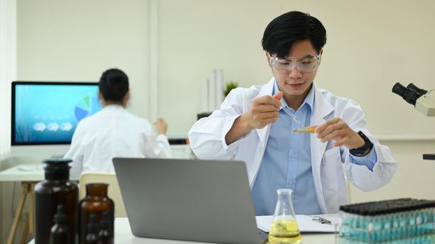Microbiologist or researcher in white coat with petri dish examining samples in research laboratory.