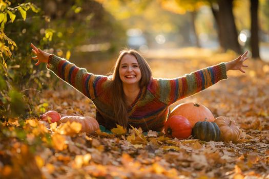 Happy woman with pumpkins lying on the yellow leaves. Cozy autumn vibes Halloween, Thanksgiving day.
