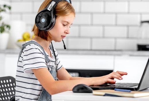 Preteen girl studying wearing headphones during online e-learning lesson with laptop. Child pupil making video call in distance educatipon coronavirus time