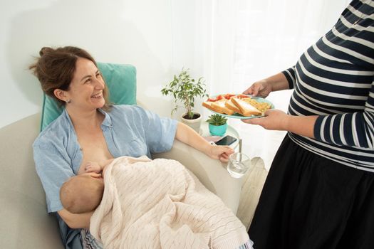 Elder woman helps to eat for new mother when she breastfeeds her baby. Motherhood support