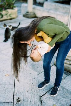Smiling mother bent over with a baby in her arms holding him above the ground. High quality photo